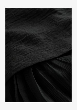 Čierna látka s textúrovaným povrchom, s hladkým horným vrstvom a plisovanou dolnou časťou, obidve v_hlbokej, jednorodnej čiernej farbe.