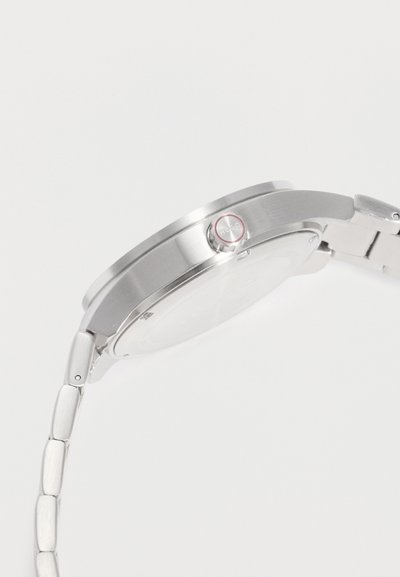 Vue latérale d'une montre-bracelet en métal argenté montrant la couronne ronde avec le logo Rado et le bracelet à maillons.