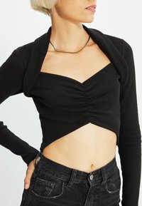 Top corto nero con texture a coste, scollatura a cuore e dettagli arricciati al centro. Abbinato a jeans neri a vita alta.