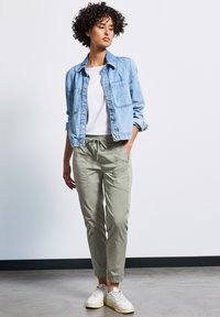 Blå denimjacka över en vit skjorta, tillsammans med ljusgröna avsmalnande byxor och vita sneakers, med elastiska mudd och fickor.