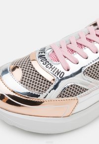 Metalické stříbrné tenisky s růžovo zlatými akcenty, síťovými panely, růžovými tkaničkami a bílou podrážkou s texturovanými detaily. Logo viditelné na boku.