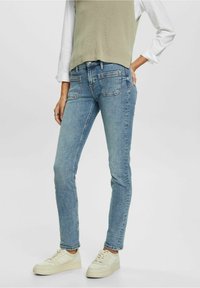 Ljust blå skinny jeans med en urtvättad finish, med en klassisk femficksdesign, i kombination med en grå ärmlös topp och ljusa sneakers.