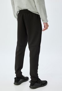 Sorte atletiske bukser lavet af glat materiale, med en tapered ben-design og elastisk livvidde, parret med sorte sneakers.