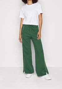 Gröna vida sweatpants med sidopiping, tillsammans med en vit t-shirt med rund hals. Outfiten fulländas med vita sneakers.