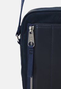 Bolso bandolera de color azul marino con un exterior de nailon texturizado, detalles de cuero suave, herrajes de cremallera plateados y costuras en contraste.