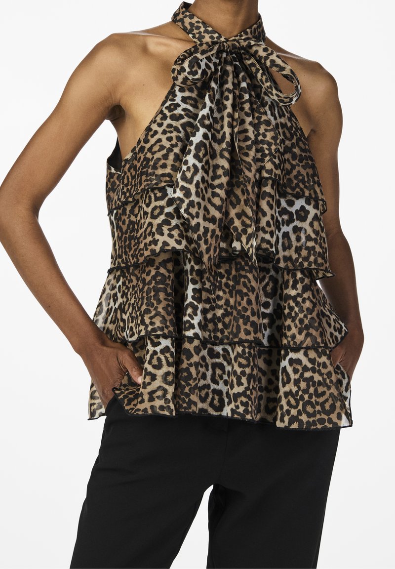 Haut à col licou imprimé léopard avec des volants superposés, présentant un détail nœud au niveau du cou et un tissu léger. Un pantalon noir est porté en dessous.