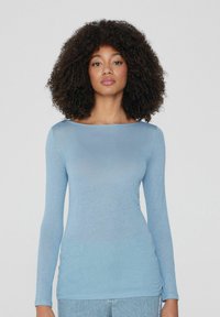 Hellblaues Langarmoberteil mit weitem Halsausschnitt. Der Stoff hat eine weiche Textur, eine figurbetonte Silhouette und einen subtilen Glanz. Betont die Figur.