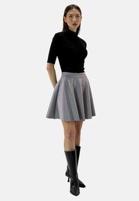 Schwarzes, figurbetontes Oberteil mit kurzen Ärmeln, kombiniert mit einem grauen, ausgestellten Rock. Das Model trägt kniehohe schwarze Stiletto-Stiefel. Einheitlicher Hintergrund.