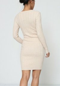 Robe en tricot beige, dotée d'une texture côtelée, de manches longues et d'une coupe ajustée. Conçue avec un col rond et des détails en tricot à torsades.