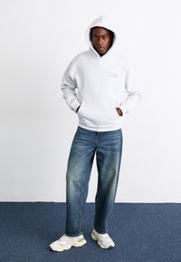 Gray hooded sweatshirt with a front pocket, paired with light blue straight-leg jeans and white athletic shoes. Simple design, no patterns.