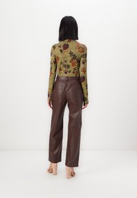 Long-sleeve green top with floral pattern, paired with high-waisted brown leather pants, featuring two back pockets and a straight fit.