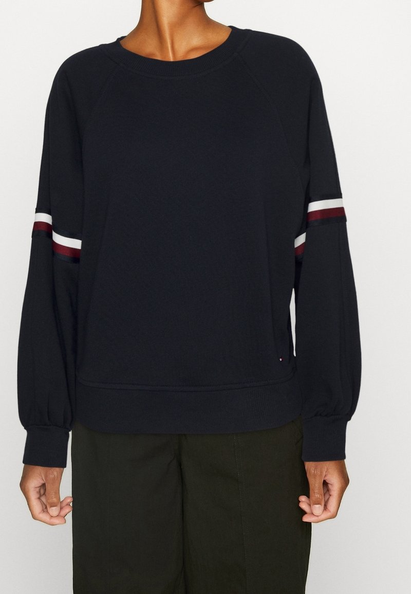 Felpa navy con maniche raglan, caratterizzata da strisce bianche e bordeaux sulle braccia. Tessuto morbido, vestibilità comoda e polsini a costine.