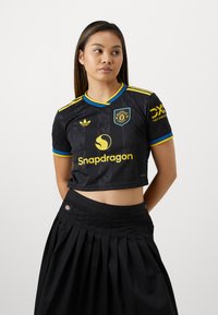 O jersey preto cortado apresenta mangas curtas, detalhes multicoloridos e um padrão texturizado. O logótipo e os detalhes de marca são proeminentes na parte da frente.