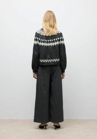 Maglione lavorato a maglia nero e grigio con motivi geometrici bianchi; abbinato a pantaloni a gamba larga grigi e sandali neri con tacco.