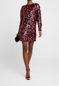 Robe ajustée à manches courtes avec un motif léopard pailleté bordeaux brillant, dotée d'un col rond et d'une silhouette droite.