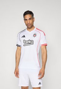 Camisa desportiva branca com detalhes em preto e vermelho, apresentando decote em V, mangas curtas e o logotipo 'Beko' na frente. Textura de tecido suave.