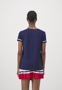 Mörkblå kortärmad topp med vita accentstrimmor på ärmarna, tillsammans med en flerfärgad plisserad kjol med röda, vita och blå strimmor.