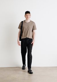Beige bomull T-skjorte med en liten logo, svarte bukser og svarte sko. Tilbehør inkluderer en svart caps og en skulderveske.