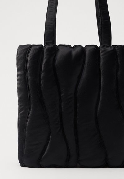 Sac fourre-tout noir en nylon rembourré avec un motif de vagues, doté de deux poignées et d'une texture lisse et brillante.