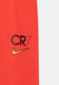 CR7 Nike shorts i lys orange stof med trykt "CR7" tekst i sort og et gult swoosh logo, glat tekstur, atletisk pasform.