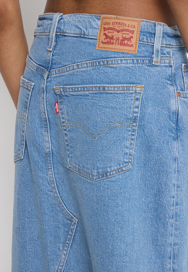 Jeans de denim azul claro con un diseño clásico de cinco bolsillos, un detalle bordado en el bolsillo trasero y una etiqueta de cuero marrón en la cintura.