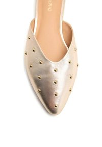 Zapato de charol dorado con punta afilada, adornado con pequeños tachuelas doradas en la parte superior, con un acabado de cuero suave.