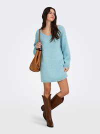 Light blue knitted sweater dress with a scoop neckline and ribbed edges. Paired with brown leather knee-high boots and a tan shoulder bag.