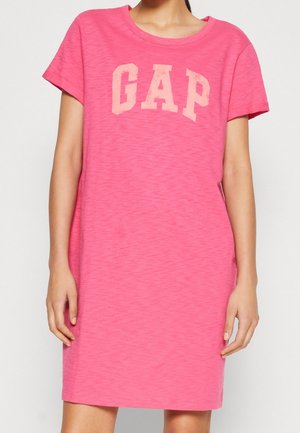 Roze T-shirtjurk met korte mouwen gemaakt van zachte stof. Heeft een lichtroze "GAP"-logo op de borst. Rechte snit.