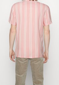 Kortärmad skjorta i ljusrosa med vita vertikala ränder, tillverkad av mjukt tyg. Har en avslappnad passform och en rundad nederkant.