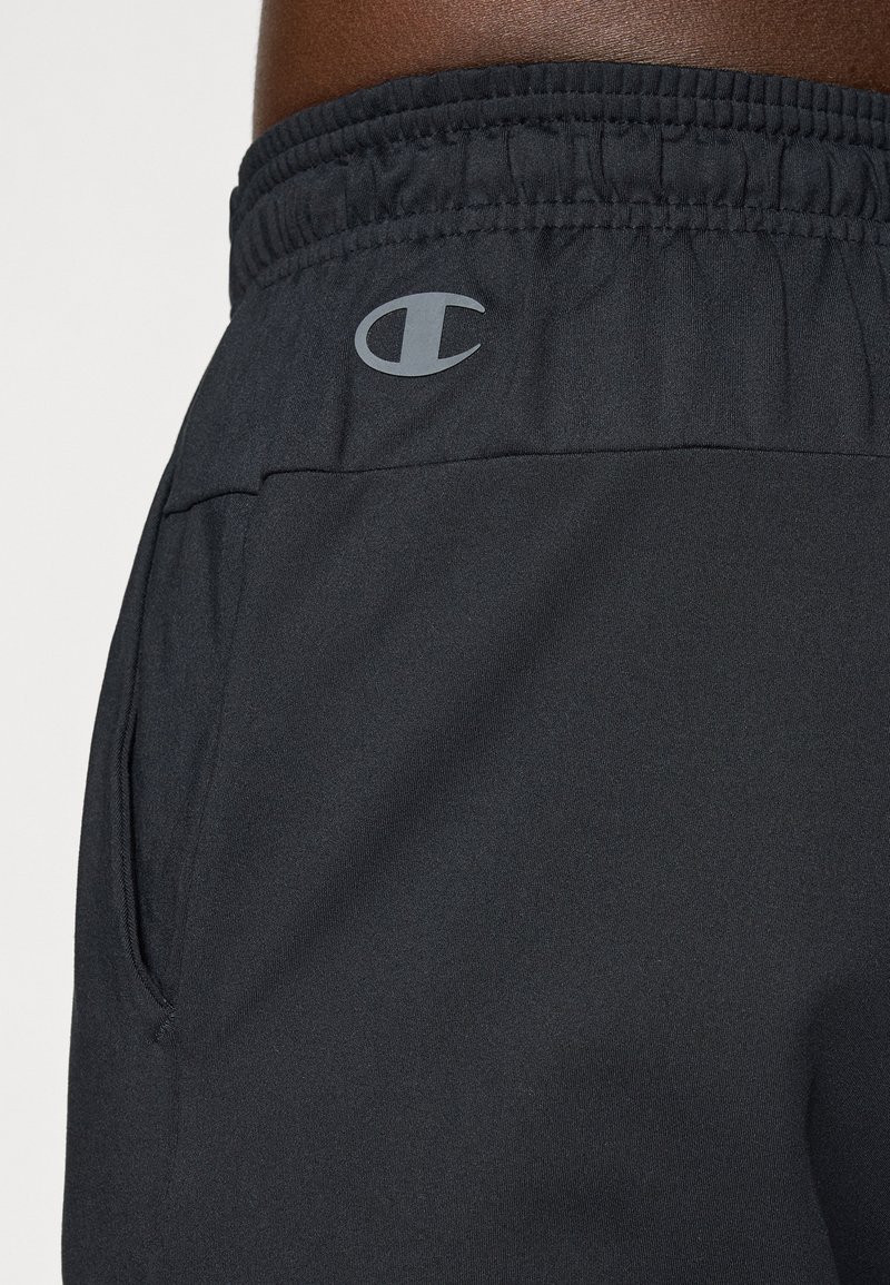 Schwarze Sportshorts mit elastischem Bund, Seitentasche und einem kleinen grauen Logo am linken Bein. Hergestellt aus leichtem Stoff.