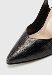 Scarpa nera con punta a stiletto, realizzata in materiale testurizzato con motivo effetto serpente, caratterizzata da un design elegante e con lato aperto.