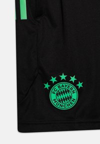 Camisa deportiva negra con acentos verdes. Presenta el emblema del FC Bayern München con un diseño circular y cinco estrellas encima del logo.