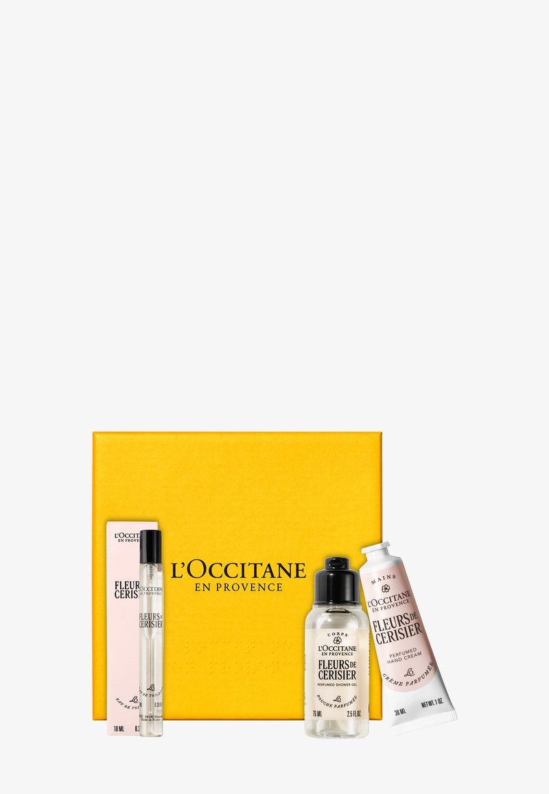 Gel douche parfumé, crème pour les mains et parfum roll-on de L'Occitane avec boîte cadeau jaune de la marque, disposés sur un fond blanc.