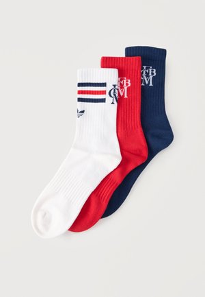 Trois chaussettes côtelées blanches type crew avec des rayures rouges et bleu marine, rouges unies et bleu marine unies, toutes avec des logos de marque blancs ou bleu marine près des bord-côtes.