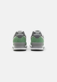Une paire de baskets New Balance vertes et grises vues de dos sur un fond blanc.