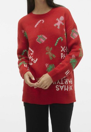 Osoba nosząca czerwony sweter świąteczny z lizakami, piernikowymi ludzikami, pudełkami na prezenty, choinkami i napisem „X-MAS PARTY”.