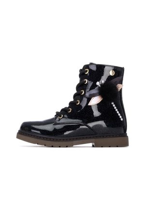Botín negro brillante con un acabado brillante, ojales dorados, cordones negros y acentos decorativos, que incluyen plumas y un pom-pom.