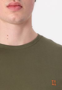 Olíva zöld pamut póló kerek nyakkivágással és rövid ujjakkal, bal mellrészen található egy kis narancssárga hímzett 'II' felirattal.