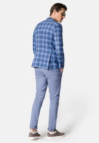 Niebieska marynarka w kratę z klapami, zestawiona z jasnoniebieskimi spodniami i szarymi trampkami. Gładki materiał z dopasowanym krojem i rozcięciem z tyłu.