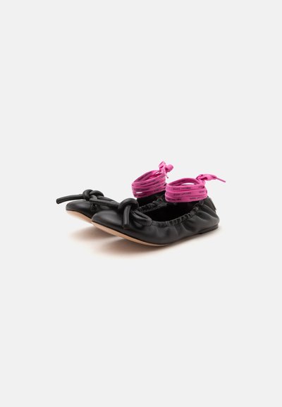 Ballerines en cuir noir avec nœuds noués et lacets rose vif autour de la cheville imprimés du nom de la marque, sur fond blanc uni.