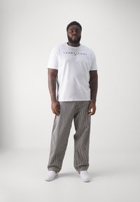 Baltas trumpomis rankovėmis marškinėliai su "TOMMY JEANS" logotipu, derinami su juodais ir baltais dryžuotais plačiakulkšniais kelniais ir baltais sportiniais bateliais.
