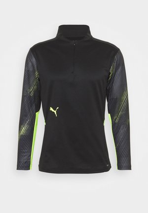 Schwarzes sportliches Langarmshirt mit einem Viertelreißverschluss am Hals. Mit grünen Akzenten und einem strukturierten Muster an den Ärmeln. Ausgestattet mit dem Puma-Logo.