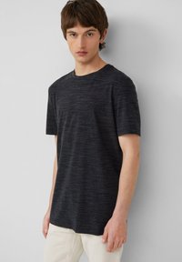 Zwarte T-shirt met korte mouwen en een gestructureerd, gemêleerd patroon. Ronde halslijn en een relaxte pasvorm. Model draagt lichte broek.