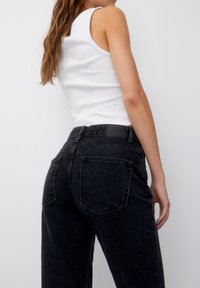 Jeans neri in denim a vita alta con una vestibilità ampia, tasche posteriori e una texture liscia, abbinati a un top in cotone bianco a coste.