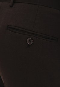 Czarne spodnie materiałowe z tylną kieszenią z zapięciem na guzik oraz płaską, teksturowaną powierzchnią. Widoczne są subtelne detale przeszyć.