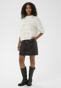 Sweater en tricot blanc avec un motif texturé, associé à une mini-jupe en cuir noire. Complété par des bottes noires hautes pour un look contrasté.