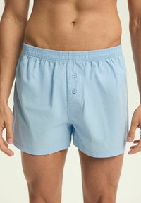 Jasnoniebieskie bawełniane szorty z elastycznym paskiem, guzikiem z przodu i luźnym krojem. Posiadają gładką teksturę i minimalistyczny design.