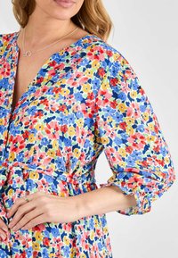 Blumenkleid mit einem mehrfarbigen Muster in Blau, Pink, Gelb und Grün; V-Ausschnitt, tailliert und mit gerafften Ärmeln.