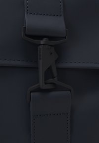 Sac à dos imperméable bleu marine avec finition mate, doté d'une boucle en plastique noir et de coutures contrastantes sur la sangle.