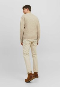 Pull en tricot beige à la coupe décontractée, associé à un pantalon crème et des bottines en daim marron, vu de dos.